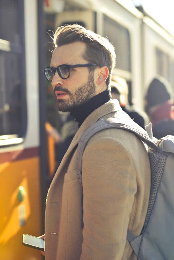 A stylish man with a backpack boards a tram in bustling Budapest, Hungary, during the day.