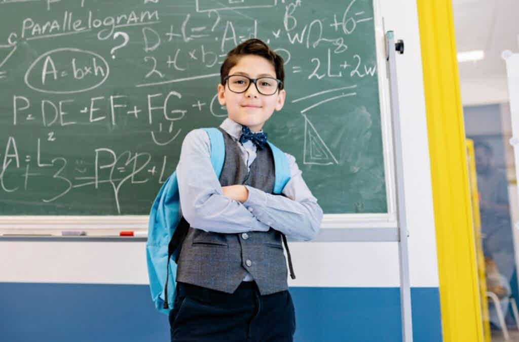 A young student stands confidently with arms crossed in front of a chalkboard filled with math equations.